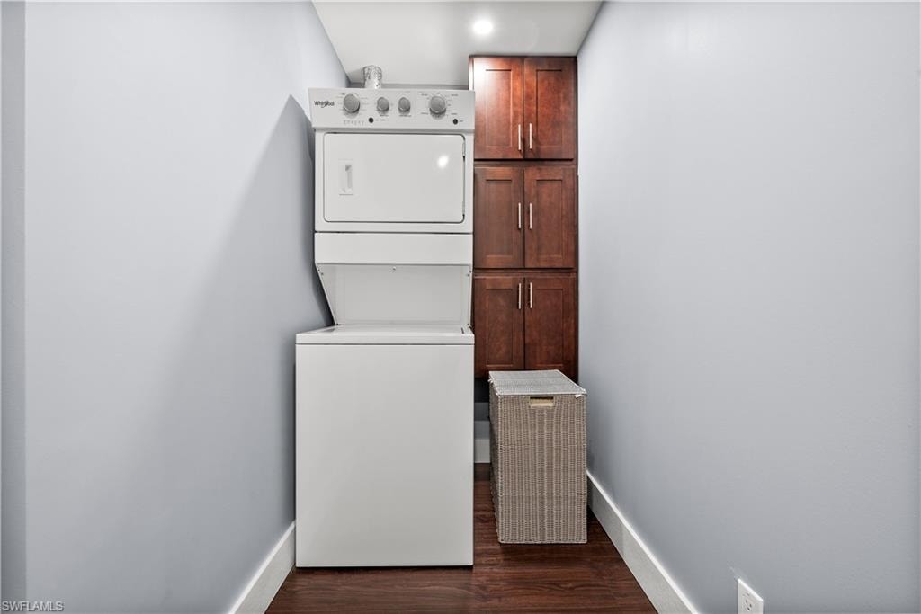 Laundry area with stacked washer / dryer, dark wood-style flooring, and cabinet space