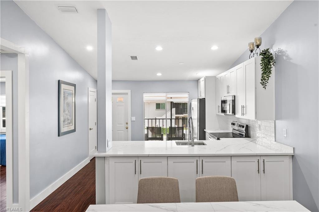 Kitchen with white cabinets, light stone countertops, stainless steel appliances, tasteful backsplash, and dark wood-type flooring