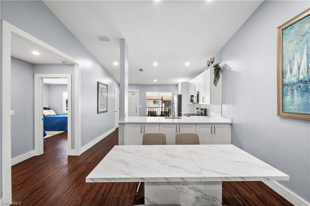 Kitchen with white cabinetry, a peninsula, dark wood-style floors, light stone counters, and stainless steel appliances