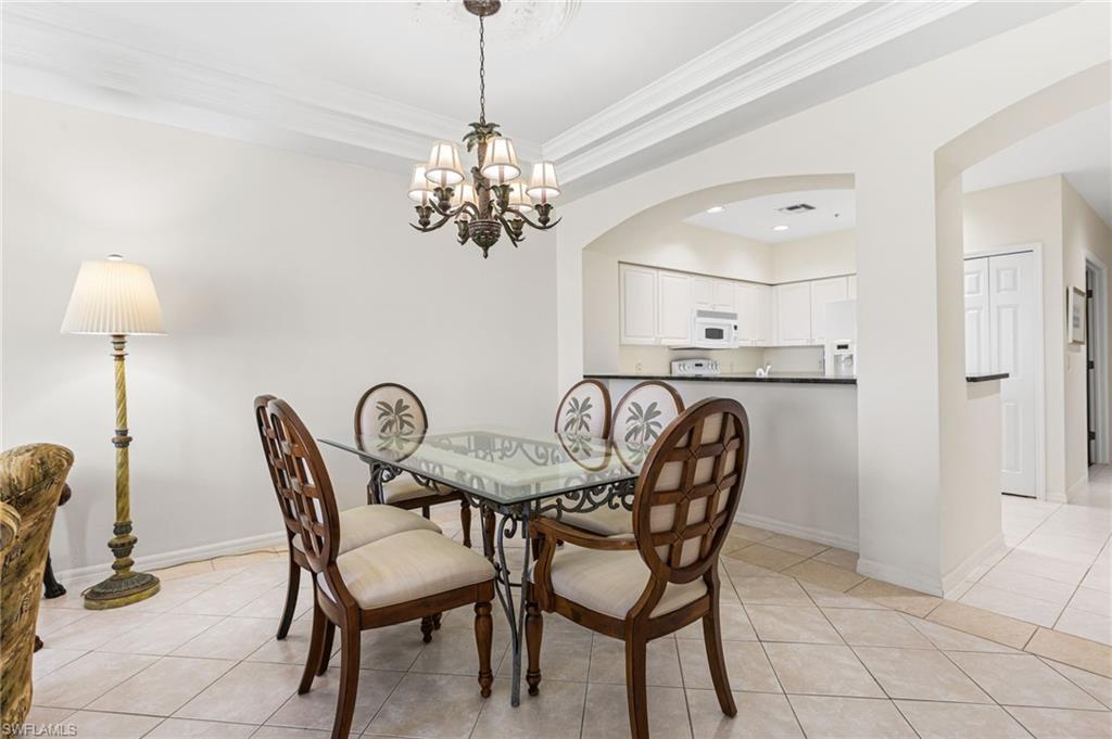 Dining room featuring light tile patterned floors, a raised ceiling, arched walkways, crown molding, and a chandelier