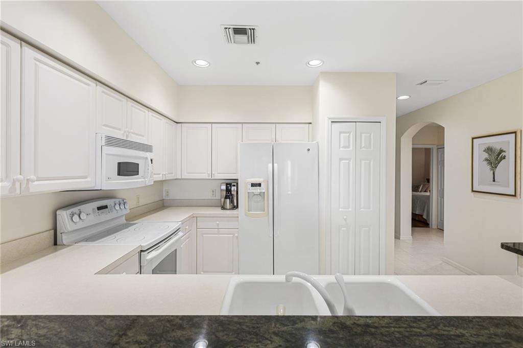 Kitchen with white appliances, white cabinetry, arched walkways, recessed lighting, and dark countertops