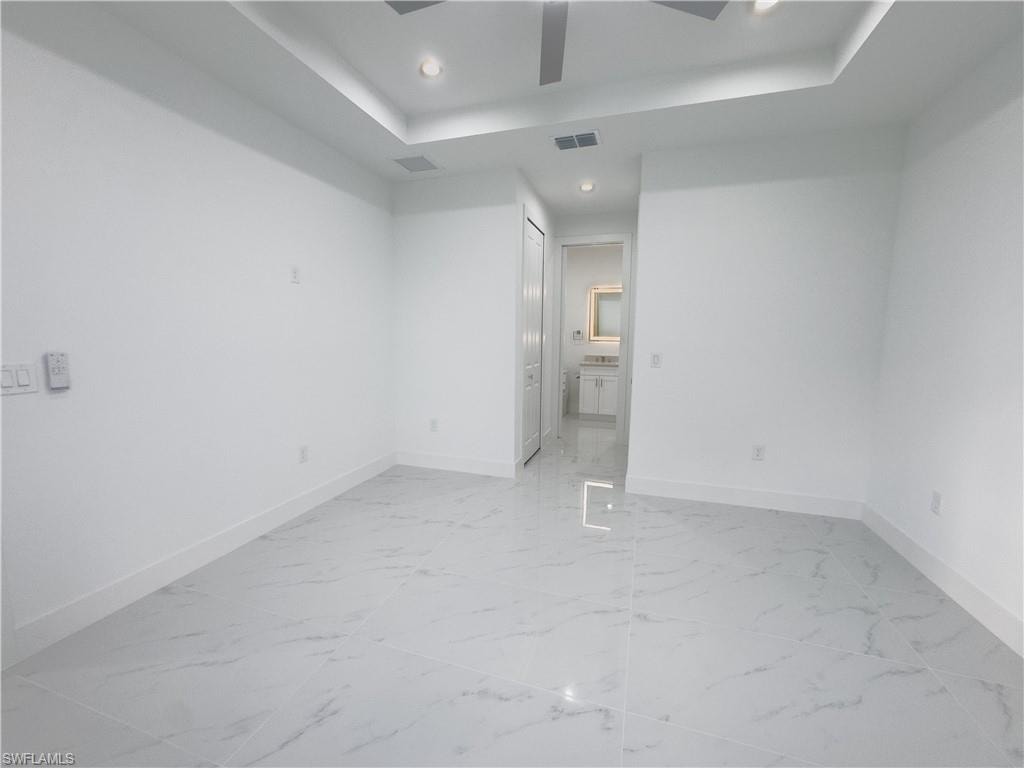 Unfurnished bedroom featuring a raised ceiling, light marble finish floors, recessed lighting, ceiling fan, and connected bathroom