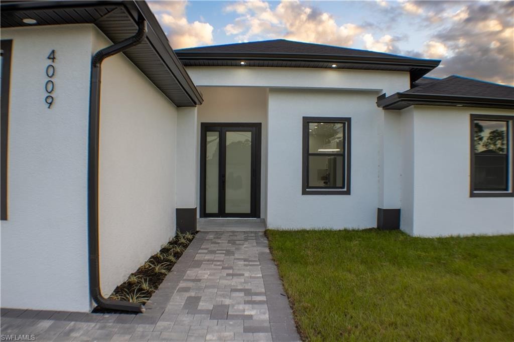 Exterior entry at dusk featuring stucco siding and a yard