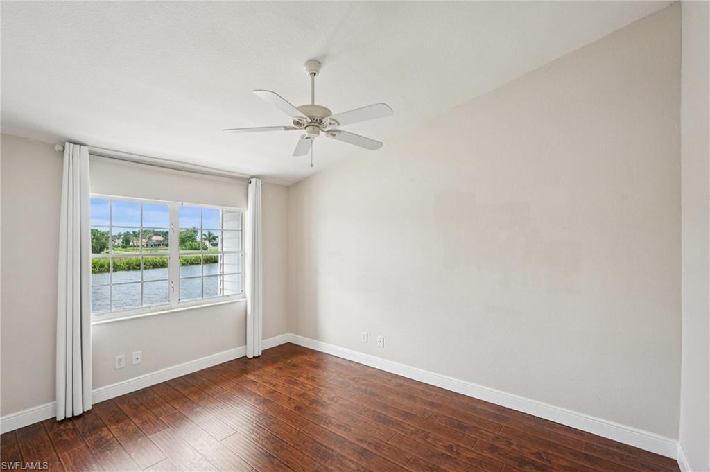 Spare room with dark wood-type flooring, a water view, lofted ceiling, and ceiling fan