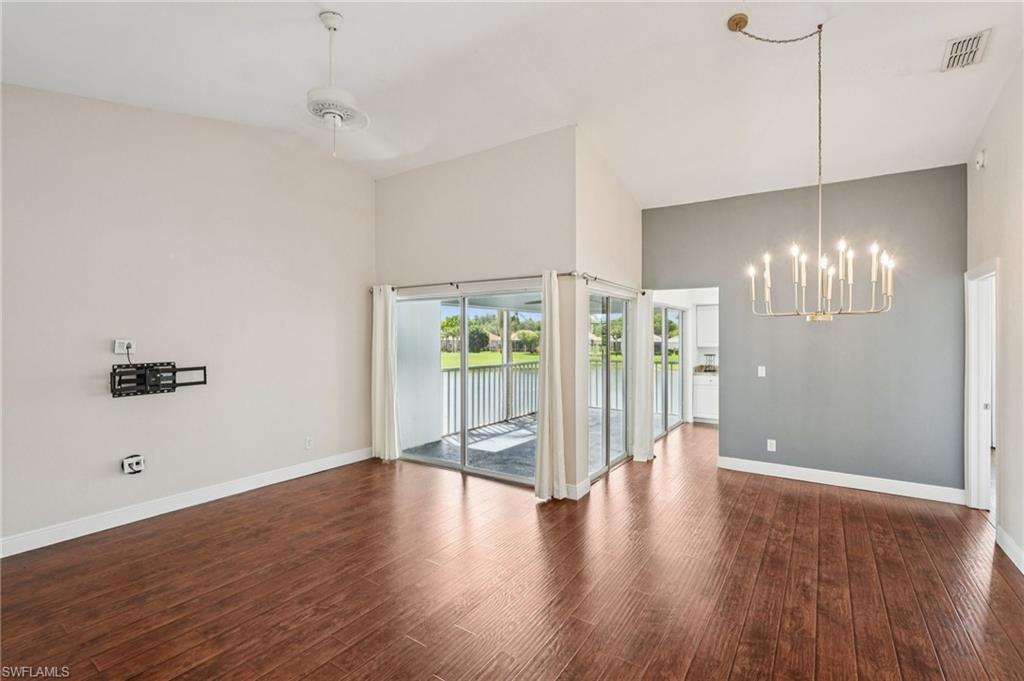 Unfurnished dining area with a chandelier, dark wood finished floors, a water view, a ceiling fan, and a high ceiling