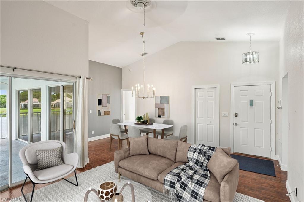 Living area with high vaulted ceiling, a chandelier, wood finished floors, and a water view