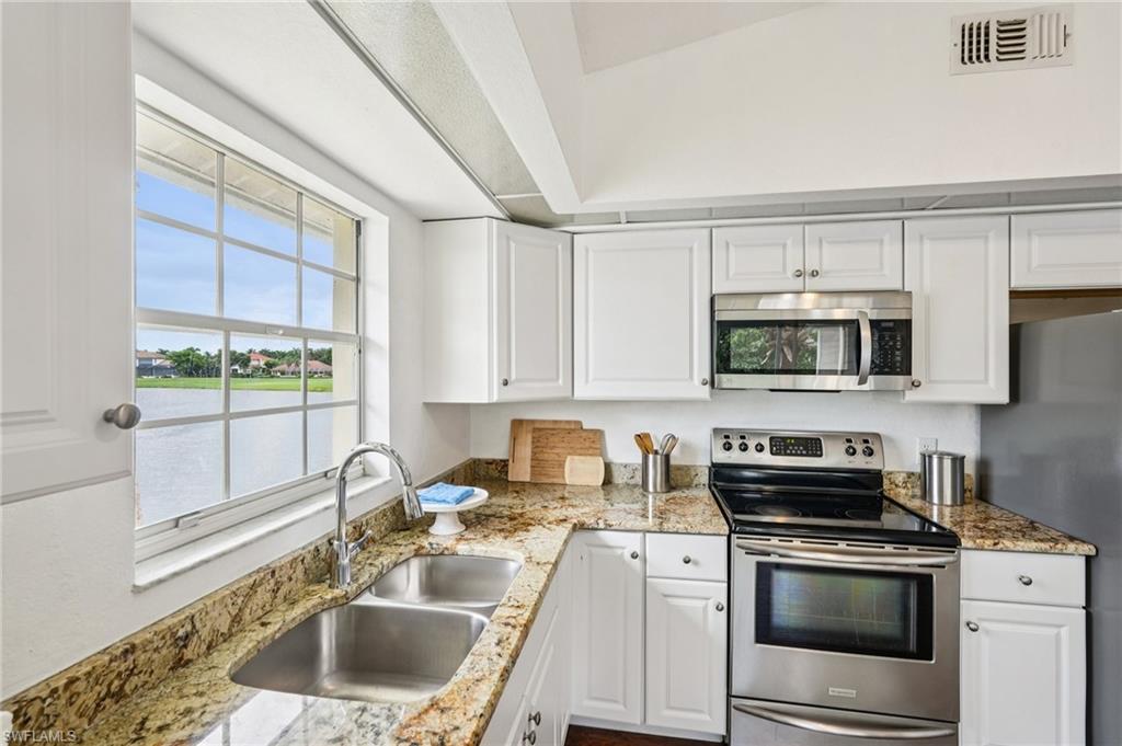 Kitchen with appliances with stainless steel finishes, white cabinetry, a water view, and light stone counters