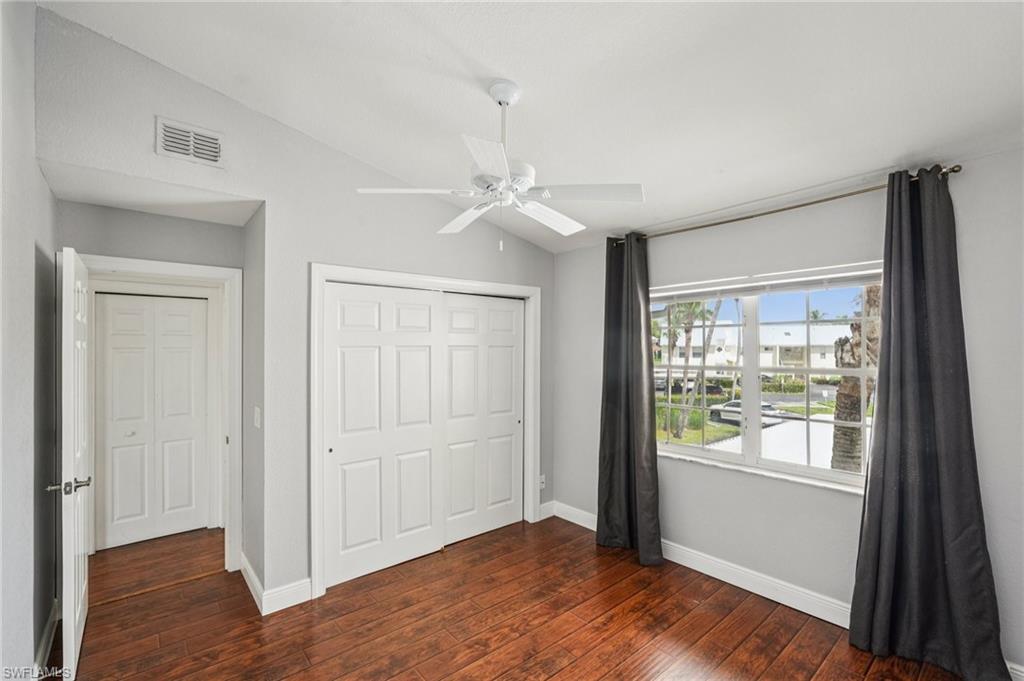 Unfurnished bedroom with lofted ceiling, a closet, dark wood-style flooring, and a ceiling fan