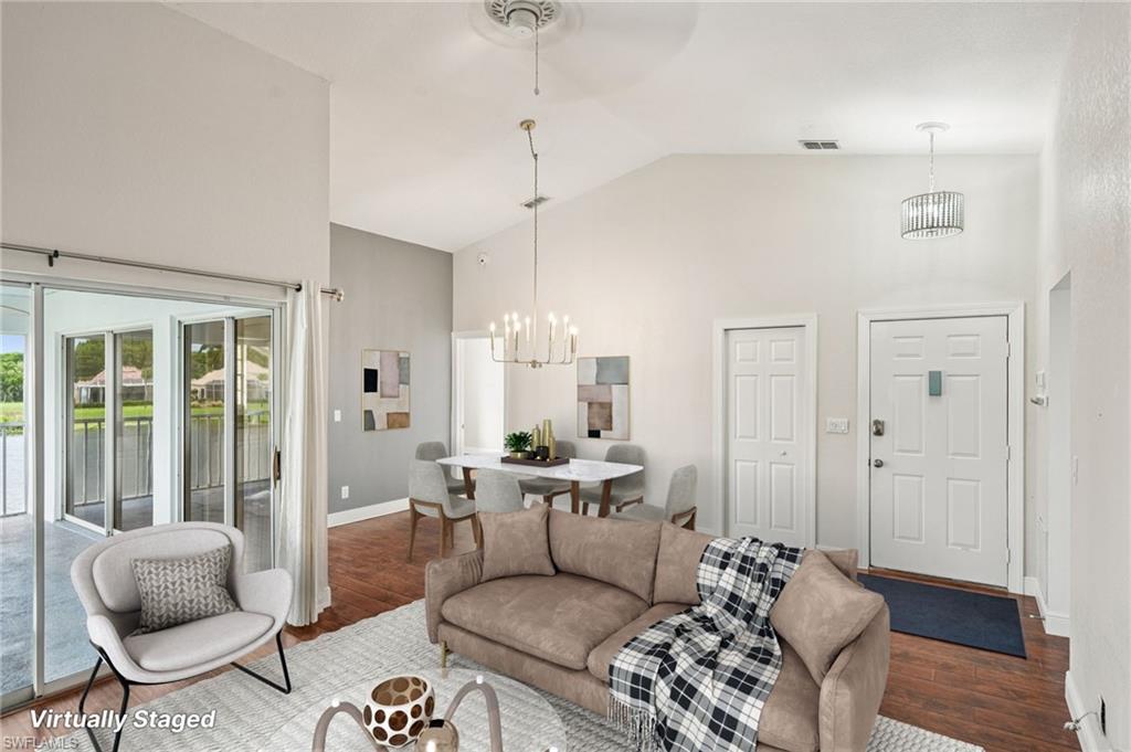 Living area with high vaulted ceiling, a chandelier, wood finished floors, and a water view