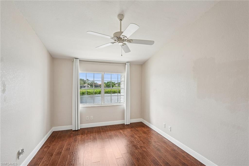 Unfurnished room featuring dark wood-style floors, a ceiling fan, a water view, and a textured wall