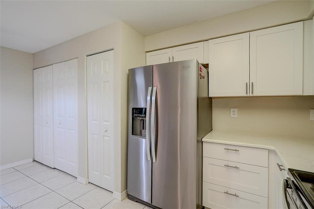 Kitchen with stainless steel fridge with ice dispenser, black range, white cabinetry, light stone counters, and light tile patterned flooring