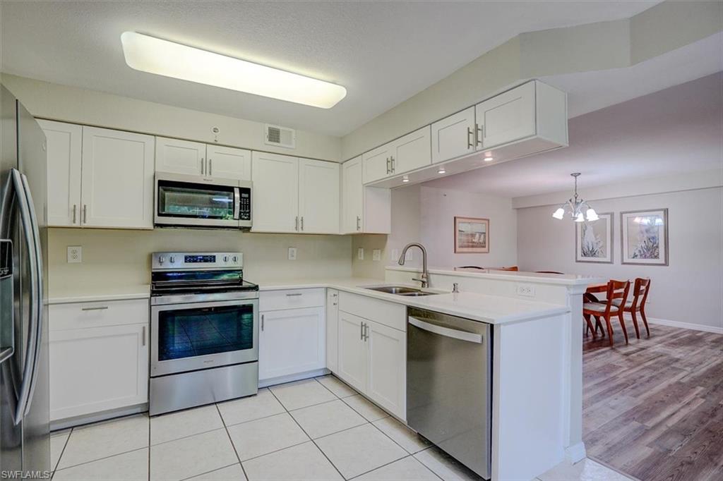 Kitchen featuring stainless steel appliances, white cabinetry, a chandelier, and a peninsula