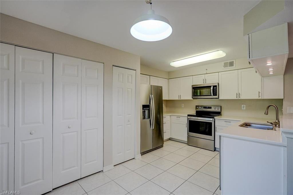 Kitchen featuring appliances with stainless steel finishes, white cabinets, light tile patterned flooring, and decorative light fixtures