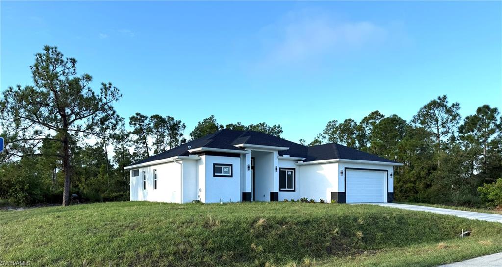 View of front of house with a front lawn, stucco siding, an attached garage, and driveway