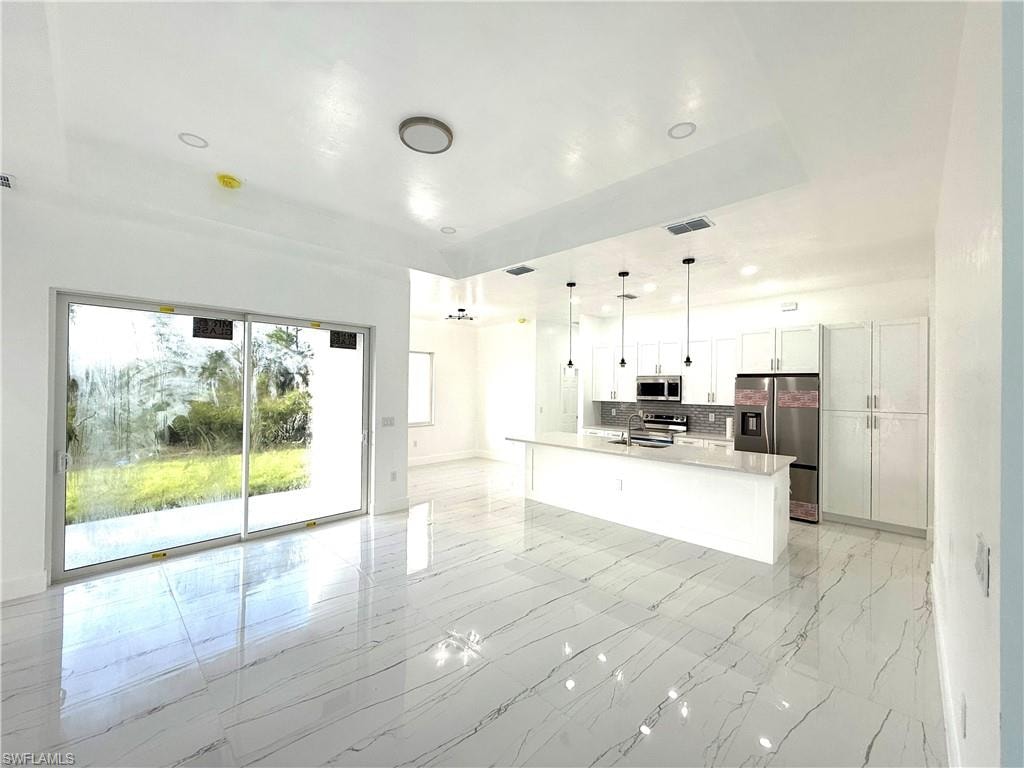 Kitchen with hanging light fixtures, white cabinetry, open floor plan, appliances with stainless steel finishes, and a spacious island
