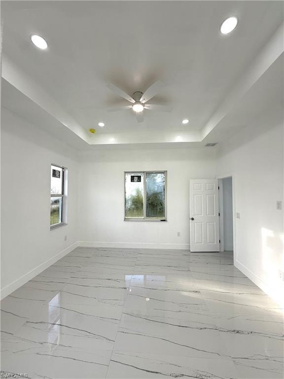 Unfurnished room with a raised ceiling, recessed lighting, light marble finish floors, and ceiling fan