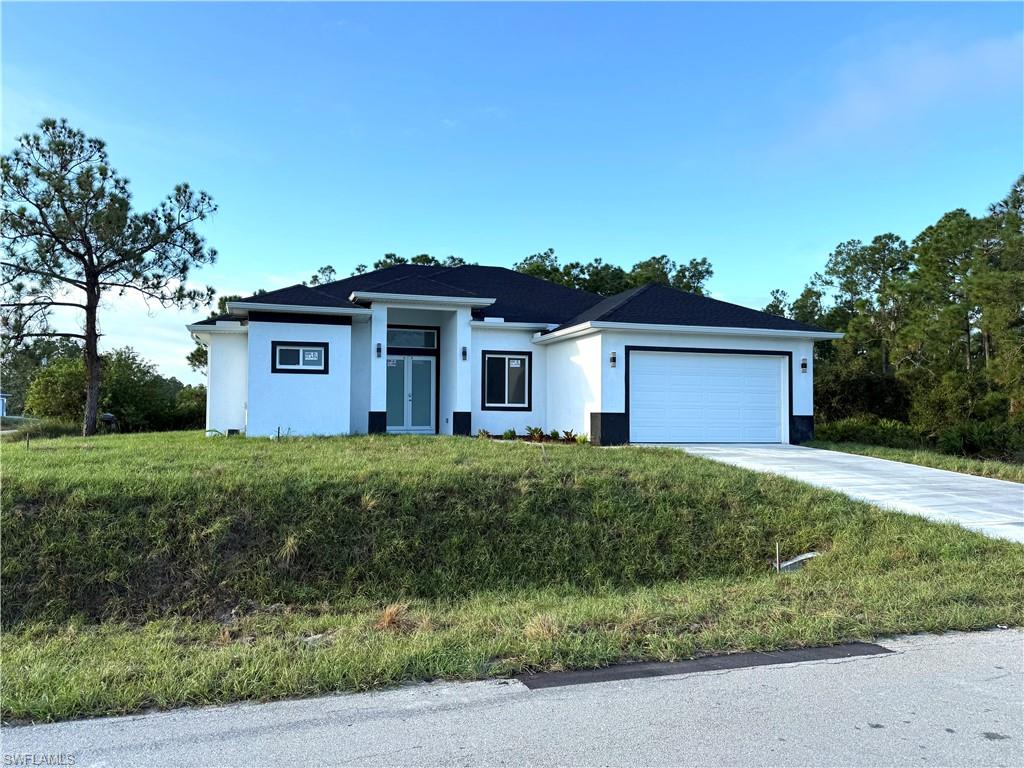 View of front of house with concrete driveway, stucco siding, an attached garage, and a front yard