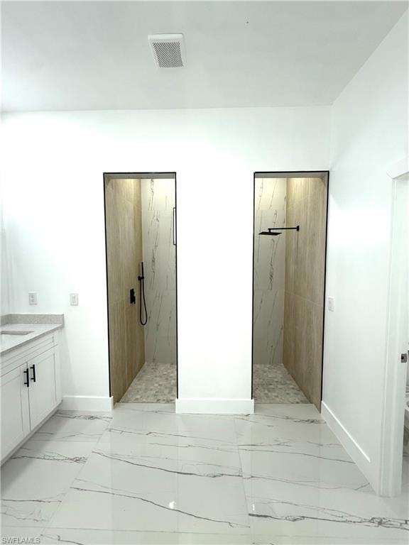 Bathroom with vanity, a marble finish shower, and light marble finish floors