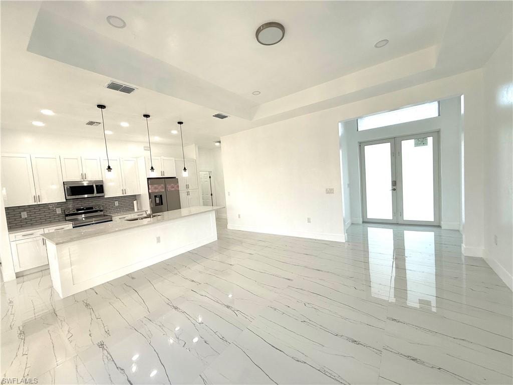 Kitchen with white cabinets, a tray ceiling, hanging light fixtures, backsplash, and recessed lighting