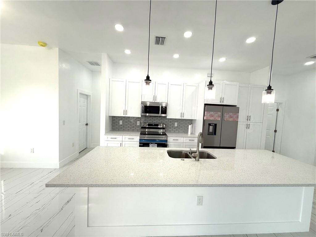 Kitchen with appliances with stainless steel finishes, backsplash, white cabinets, light stone countertops, and recessed lighting