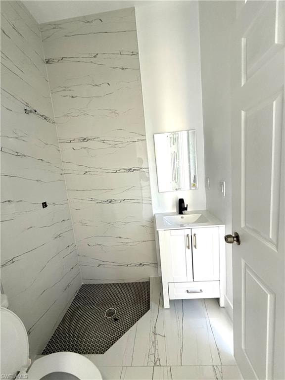 Full bath featuring a marble finish shower, vanity, and light marble finish floors