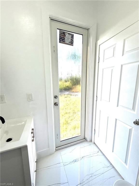 Doorway to outside with marble finish floors and a sink