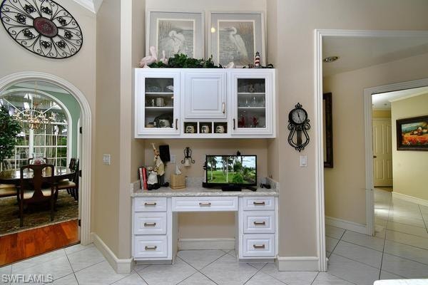 Bar featuring glass insert cabinets, light tile patterned floors, white cabinets, and built in desk