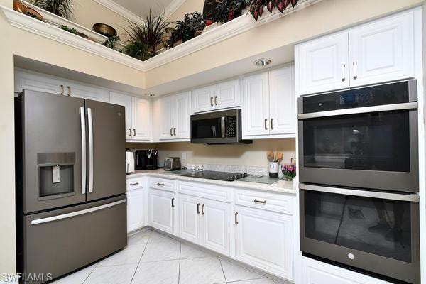 Kitchen with stainless steel appliances, white cabinets, light tile patterned flooring, and ornamental molding