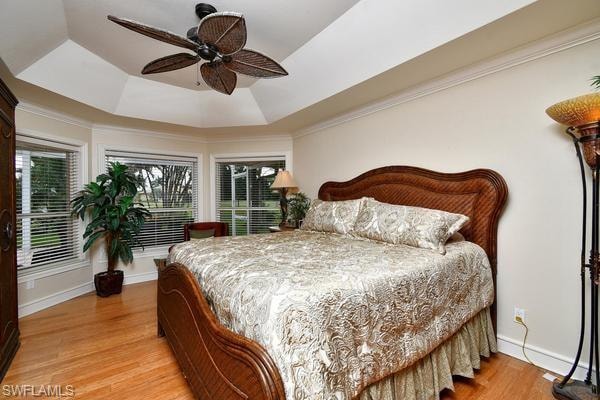 Bedroom featuring a tray ceiling, crown molding, light wood-style flooring, and a ceiling fan