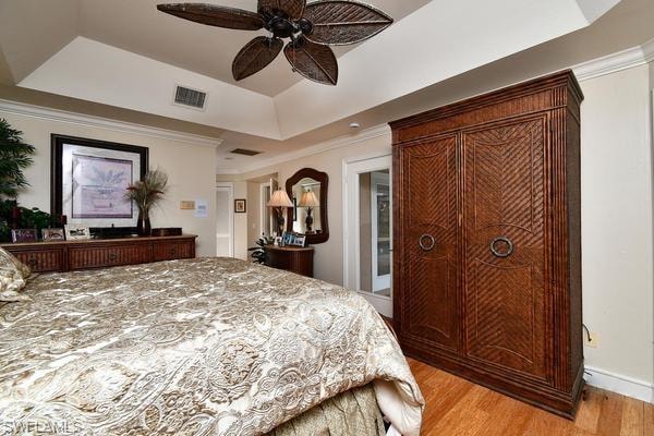 Bedroom with a tray ceiling, crown molding, light wood-style floors, and a ceiling fan