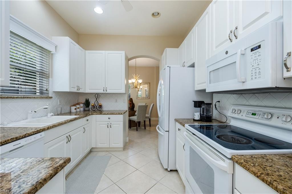 Kitchen with white appliances, white cabinetry, light tile patterned flooring, tasteful backsplash, and arched walkways