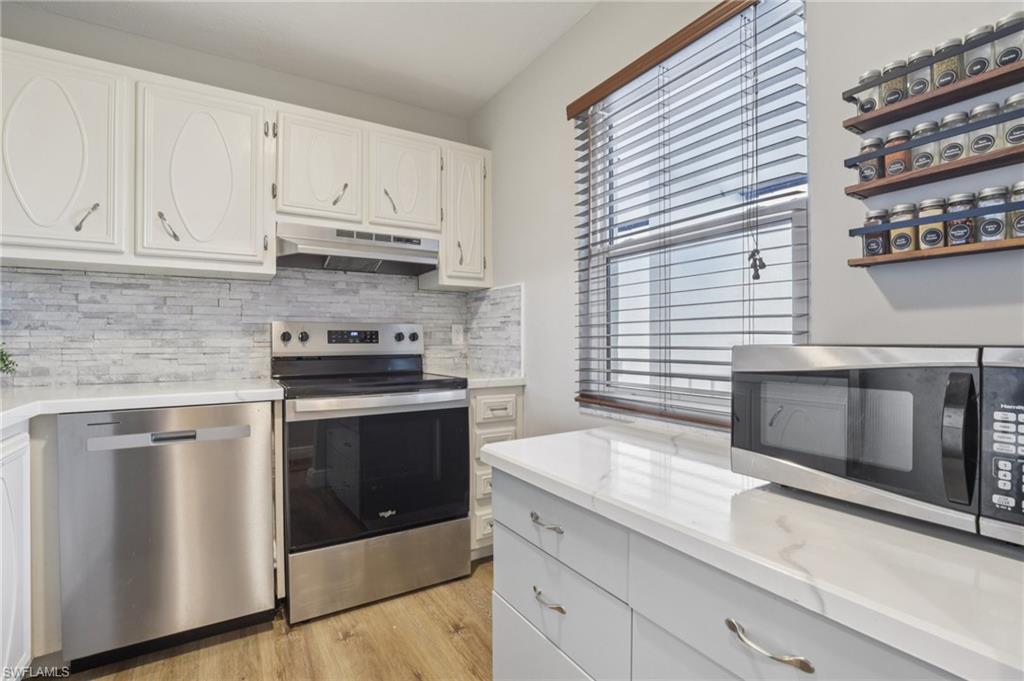 Kitchen with appliances with stainless steel finishes, decorative backsplash, white cabinets, under cabinet range hood, and light wood-style floors
