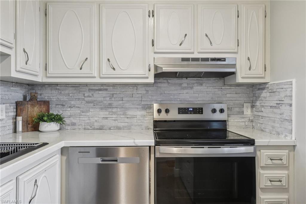 Kitchen with appliances with stainless steel finishes, backsplash, white cabinets, and under cabinet range hood