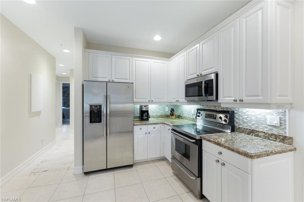 Kitchen with white cabinets, backsplash, appliances with stainless steel finishes, and light tile patterned flooring