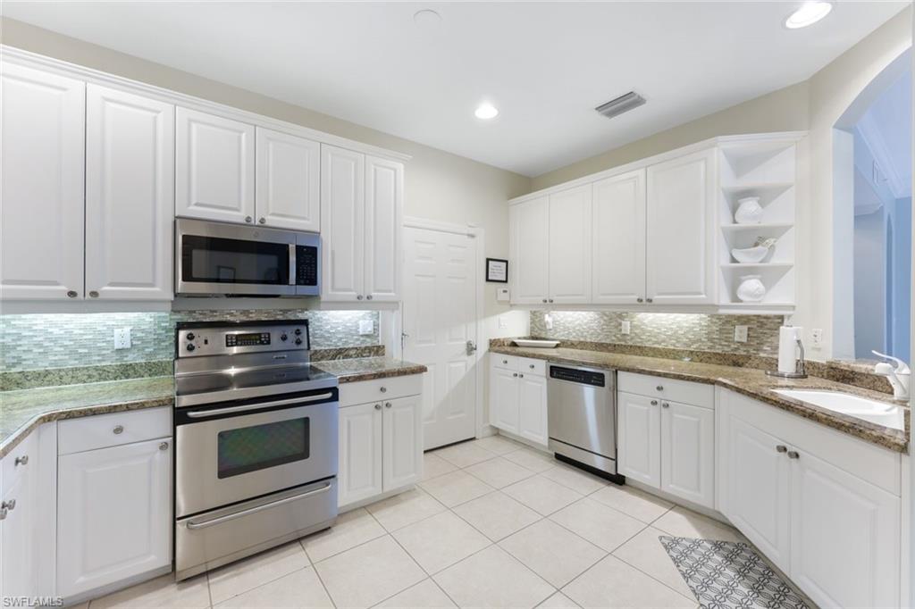 Kitchen featuring light tile patterned flooring, sink, white cabinetry, stainless steel appliances, and backsplash