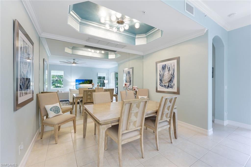 Tiled dining space featuring ceiling fan, a tray ceiling, and crown molding
