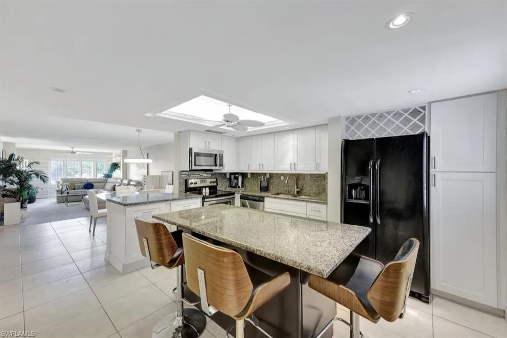 Kitchen featuring stainless steel appliances, ceiling fan, a peninsula, light stone counters, and a kitchen breakfast bar