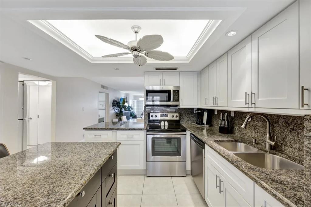 Kitchen with a tray ceiling, white cabinets, stainless steel appliances, dark stone counters, and recessed lighting