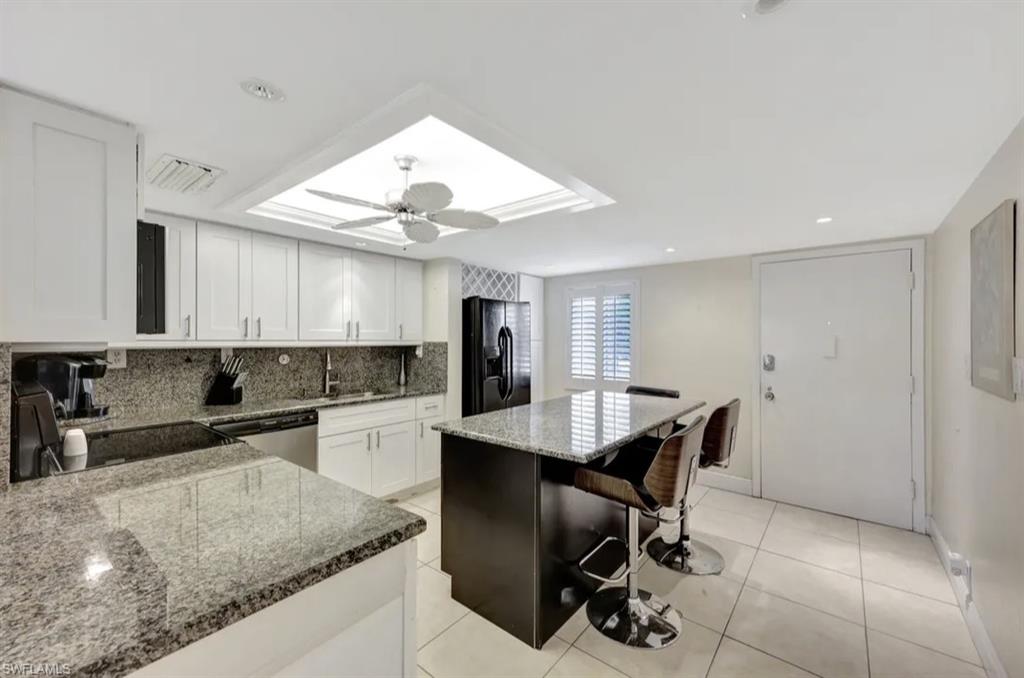 Kitchen with a kitchen breakfast bar, dark stone countertops, white cabinetry, tasteful backsplash, and black appliances