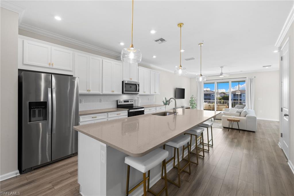 Kitchen featuring appliances with stainless steel finishes, a breakfast bar, white cabinetry, a center island with sink, and decorative light fixtures