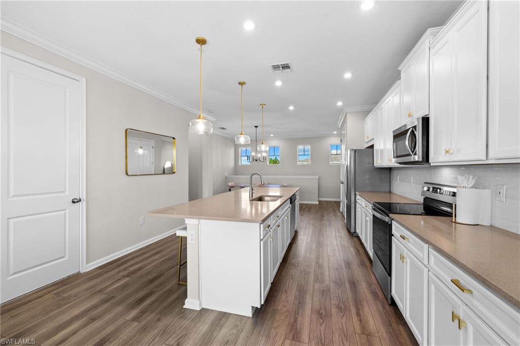 Kitchen featuring stainless steel appliances, white cabinets, a kitchen island with sink, a kitchen breakfast bar, and backsplash