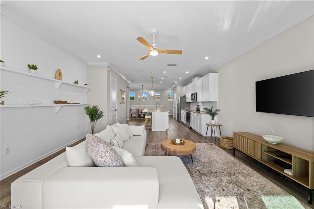 Living room with dark wood-type flooring, ornamental molding, ceiling fan, and recessed lighting