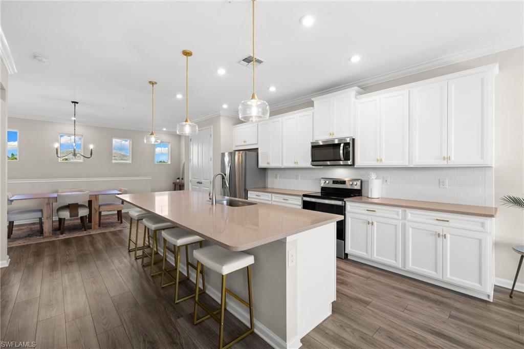 Kitchen with a breakfast bar area, stainless steel appliances, an island with sink, hanging light fixtures, and decorative backsplash