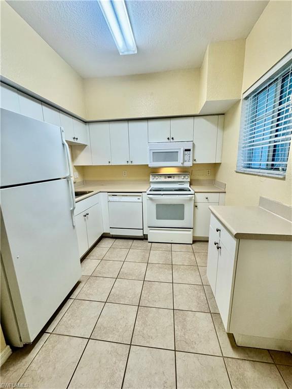 Kitchen featuring white appliances, white cabinets, light countertops, a textured ceiling, and light tile patterned flooring