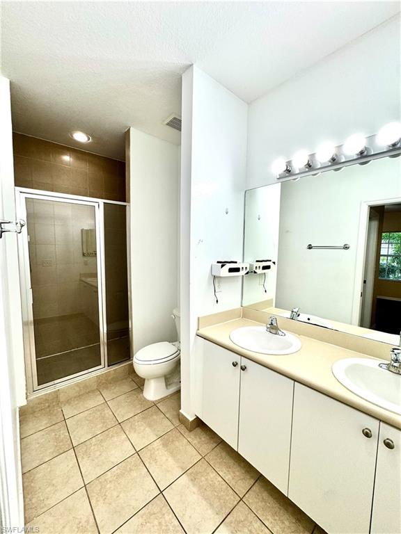 Bathroom featuring light tile patterned floors, double vanity, a stall shower, and a textured ceiling