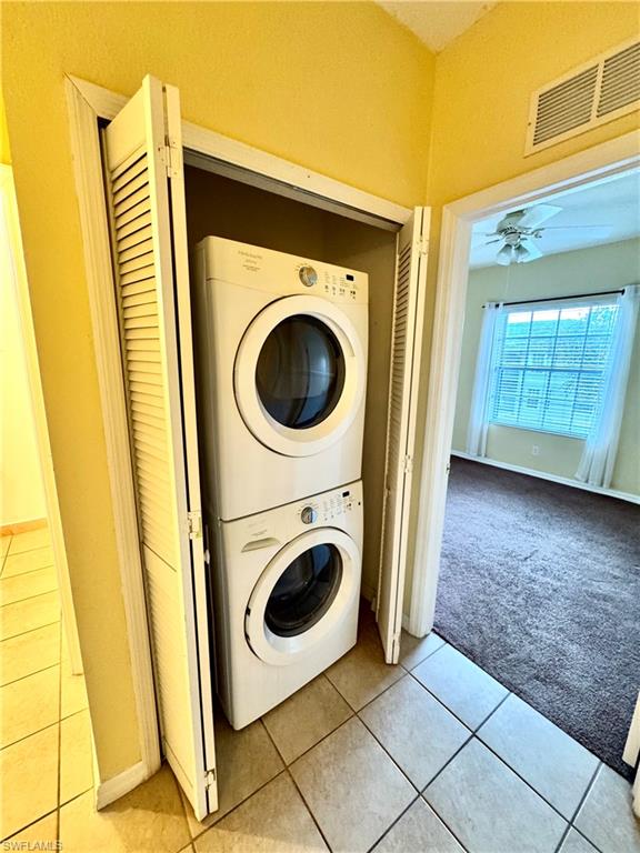 Washroom featuring light tile patterned floors, stacked washer and clothes dryer, and light carpet