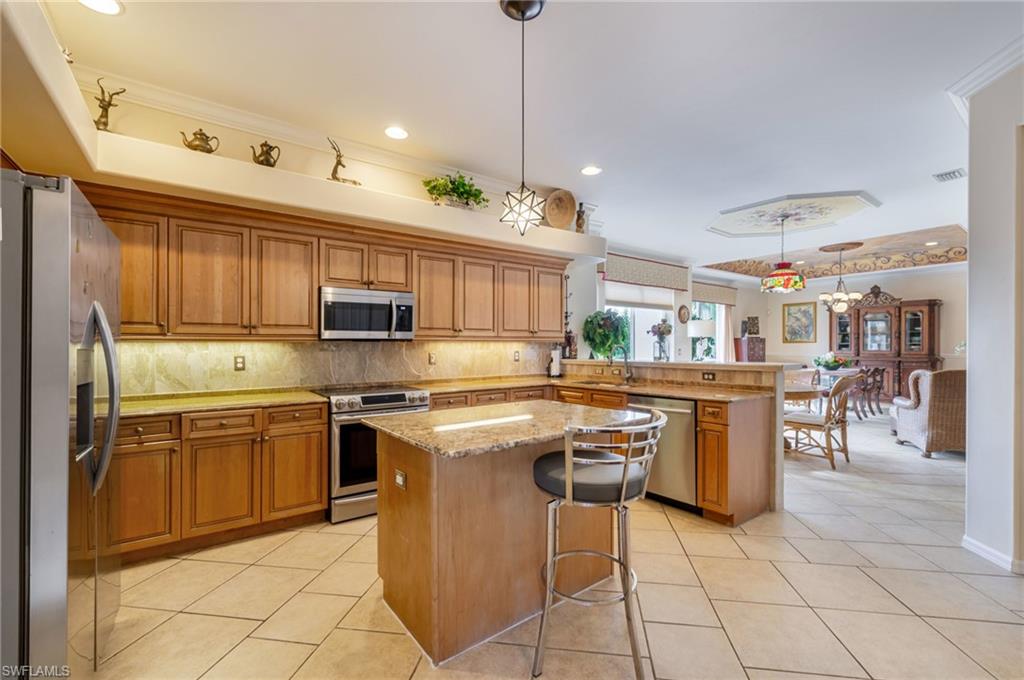 Kitchen with hanging light fixtures, backsplash, brown cabinetry, appliances with stainless steel finishes, and a peninsula