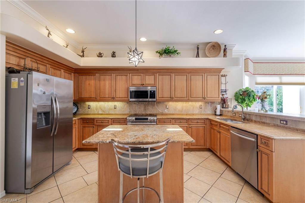 Kitchen with stainless steel appliances, decorative backsplash, light stone counters, a kitchen island, and decorative light fixtures