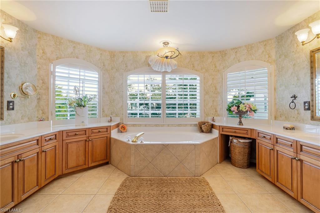 Bathroom featuring wallpapered walls, a garden tub, two vanities, and light tile patterned floors