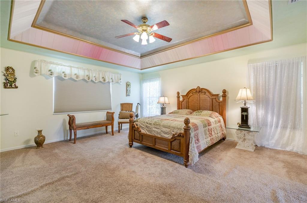 Carpeted bedroom with a tray ceiling and a ceiling fan